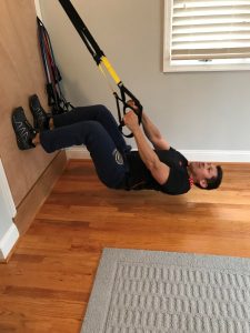 A man is doing suspension training in the house.